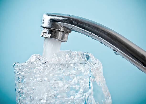 Close-up of water faucet pouring into overflowing glass stock photo