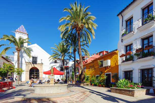 Color and bright yard with old white church and beautiful houses among green palms Marbella, Spain - December 2017: Color and bright yard with old white church and beautiful houses among green palms spanish flower pots stock pictures, royalty-free photos & images
