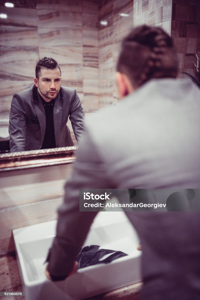 Homme d’affaires en colère debout dans les toilettes et en regardant de miroir - Photo de Miroir libre de droits