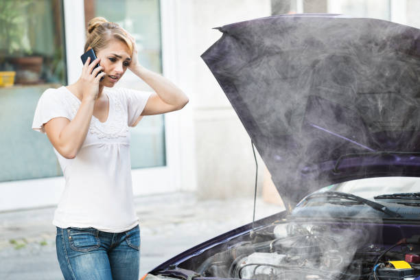 Woman Using Mobile Phone While Looking At Broken Down Car Young woman using mobile phone while looking at broken down car on street overheated photos stock pictures, royalty-free photos & images