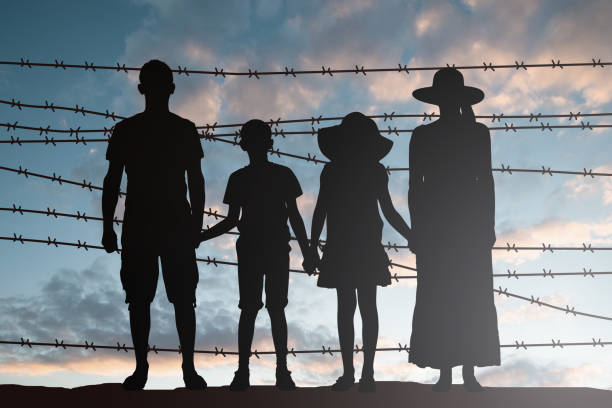 Silhouette Of Refugee Family Standing Near Fence