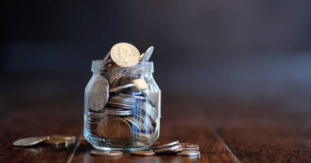 Coins in a glass jar on a wooden floor. Pocket savings from coin Coins in a glass jar on a wooden floor. Pocket savings from coins in the bank. Piggy bank in a glass jar with coins. deposit bottle stock pictures, royalty-free photos & images