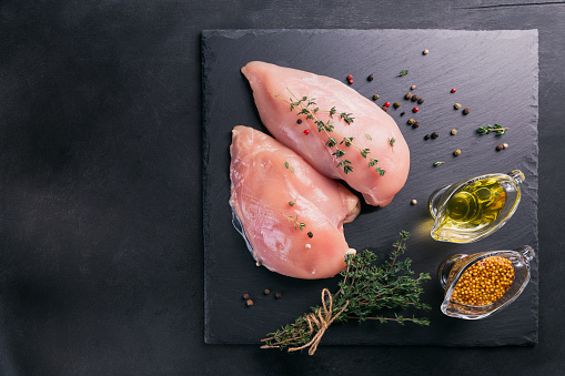 Raw chicken fillets on black cutting board with spices and herbs. Cooking ingredients. Natural healthy food concept. Flat lay with space for text