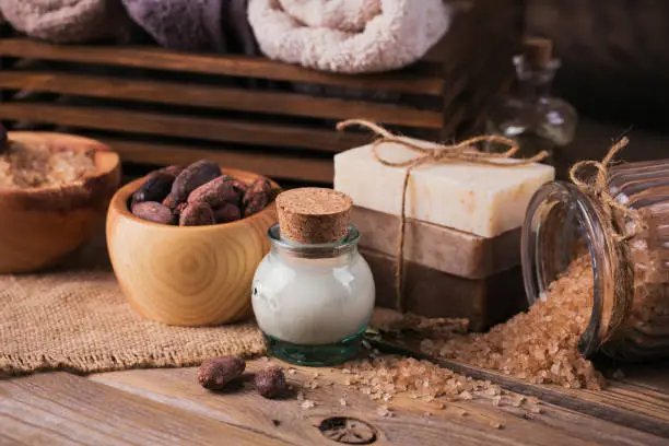 Natural cosmetic oil, cacao butter, sea salt and natural handmade soap with cocoa beans on rustic wooden background. Healthy skin care. SPA concept.