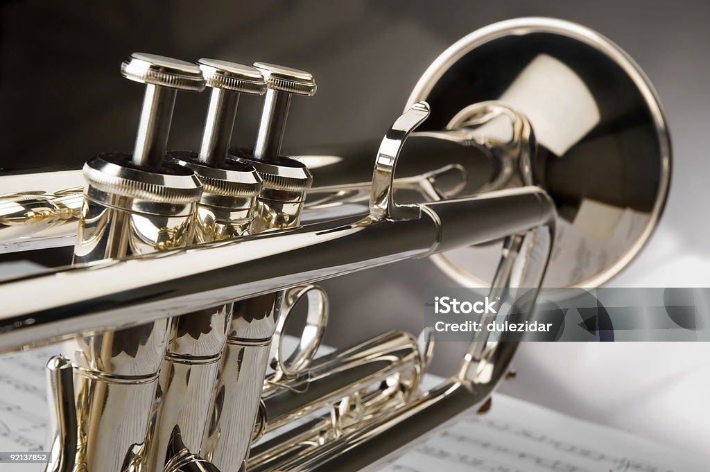 Close-up of polished trumpet sitting atop a sheet of music Trumpet on musical notes as background close up Trumpet Stock Photo
