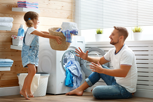 Happy family man father  householder and child daughter in laundry with washing machine