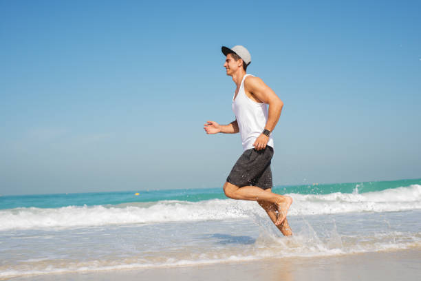 istock Young sporty man running along beautiful beach, looking happy. 921432354
