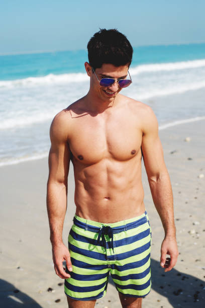 istock Young muscular man walking down the beach. Summertime chill. 921437700