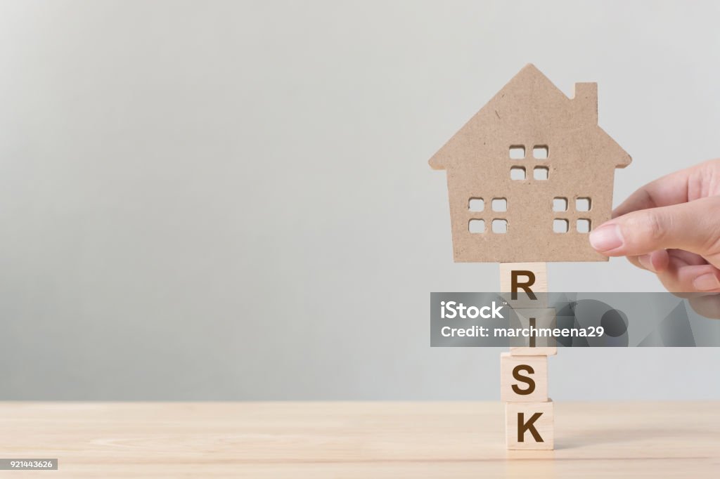 Property investment and house mortgage financial. Risk management concept. Hand putting wooden home on wood block with word "risk" Risk Stock Photo
