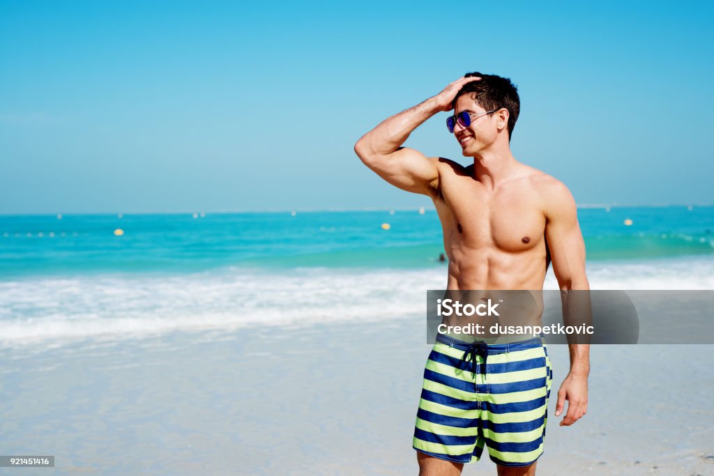 Handsome shirtless muscular fitness man at the beach, looking aside and smiling. Men Stock Photo