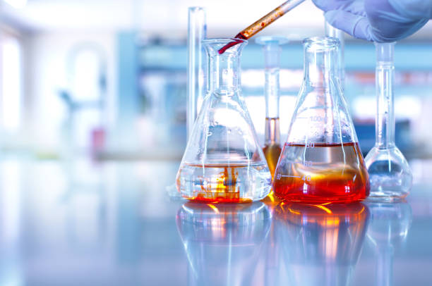 istock glass flask with hand of scientist drop orange solution in blue chemistry science research laboratory background 921472532