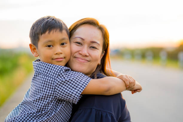 Asian mom hug her young son lovingly at sunset with nature background stock photo