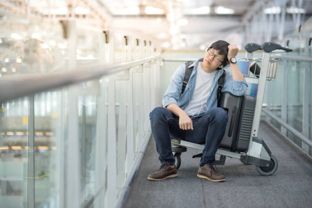 Young Asian man feeling exhausted sitting on trolley in airport terminal