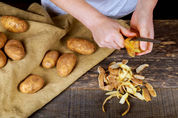 kobieta ręce skórki ziemniaków, peelingi na drewnianej deski do krojenia. trzy czyste ziemniaki na talerzu. - root vegetable raw potato human skin root zdjęcia i obrazy z banku zdjęć