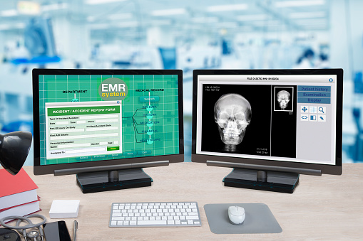 Health information and patient x-ray show on two computer monitors on doctor desk with blue background of hospital office.