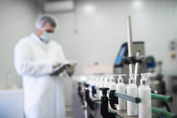 close up van vloeibare zeep, gaande van een productielijn voor cosmetica stof werknemer te typen op een tablet. - farmaceutische fabriek stockfoto's en -beelden