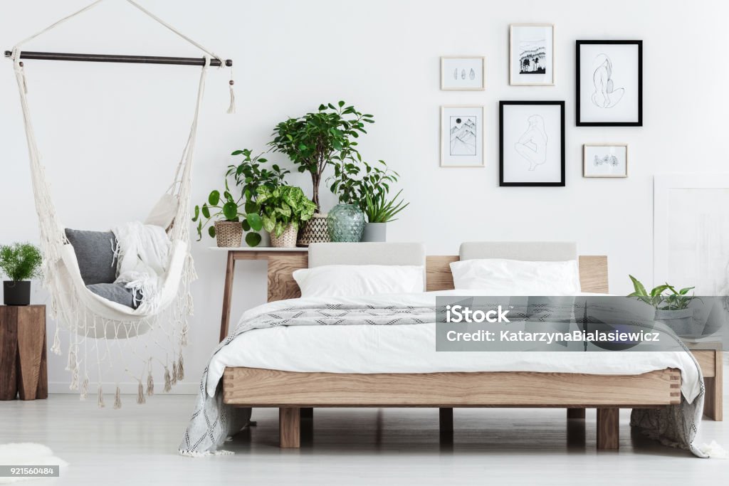 Natural bedroom with plants Plants behind wooden bed near hammock with pillows in natural bedroom with posters on white wall Bedroom Stock Photo