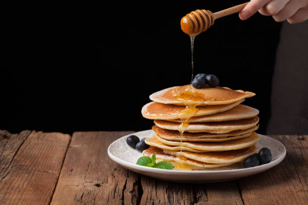 istock The chef pours honey pancake stack with blueberries and mint on black background. Copy space for your text 921570934