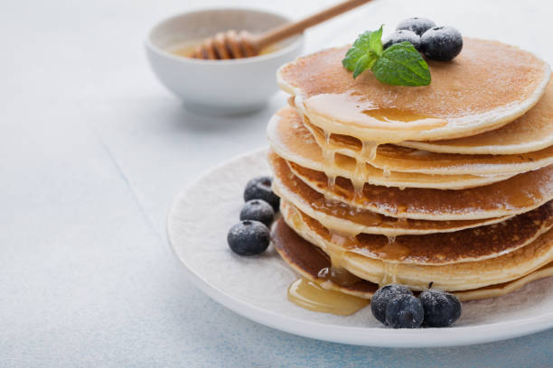 istock A stack of delicious pancakes with honey and blueberries on a light blue background. with copy space 921570952