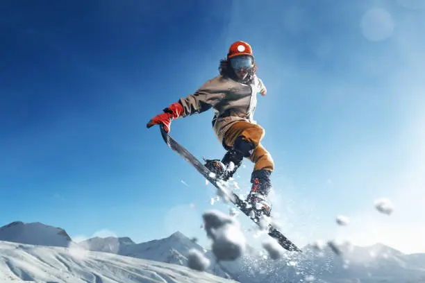 Male extreme snowboarder jumps and do a spectacular stunt in the air against a background of blue skies and snowy mountains. Freestyle snowboarding.