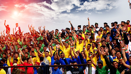 Rohtak, Haryana, India – January 26, 2017: Ecstatic group of people  of Indian ethnicity standing in the stadium during sunrise wearing casual clothing during sports event happening in the ground or stadium and all people looking cheerful with arms outstretched while standing in the stadium at the time of sports event.