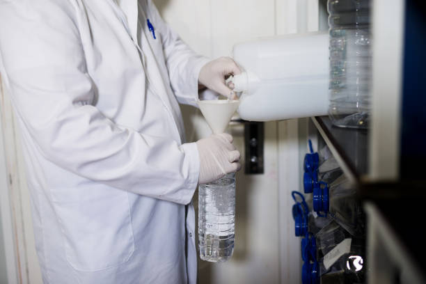 istock Fabric professional worker in uniform pouring liquid from a plastic canister to bottle through the funnel in fabric storehouse. 921574388