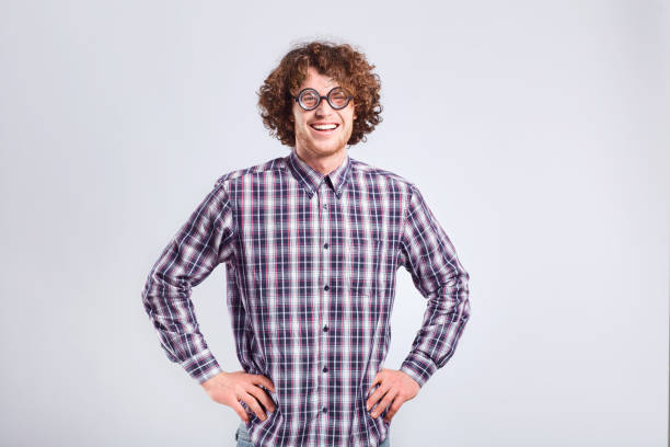 Curly nerd man in glasses with a stupid kind of funny emotion on a gray background.
