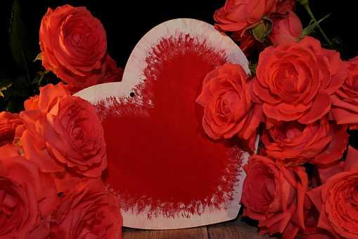 beautiful pink rose and heart figurine on black background on wooden boards