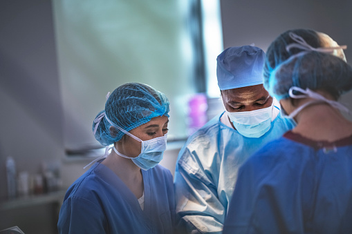 Multi-ethnic surgeons working at operating room at hospital. Team of doctors are standing in emergency room. They are wearing blue scrubs.