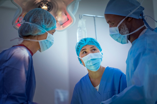 Multi-ethnic surgeons discussing at operating room. Doctors are working in emergency room at hospital. They are wearing blue scrubs.