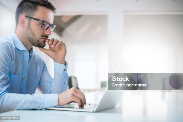 Retrato De Hombre Joven Sentado En Su Escritorio En La Oficina Foto de stock y más banco de imágenes de Ordenador portátil