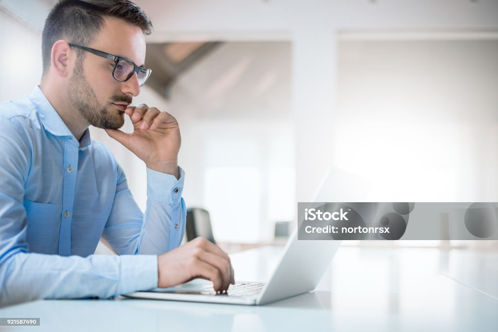 Portrait of young man sitting at his desk in the office Laptop Stock Photo