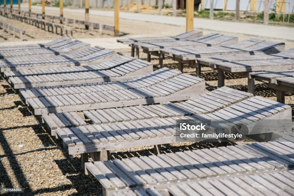 Close-up wooden sun loungers on a pebbled public beach by the seashore. Side view. Close-up wooden sun loungers on a pebbled public beach by the sea. Side view. Beach Stock Photo