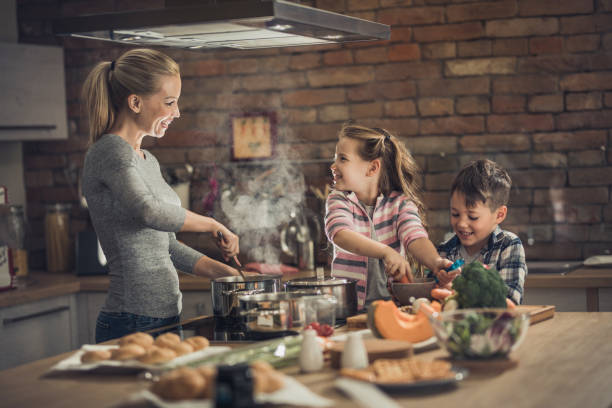 Happy single mother talking to her kids while preparing lunch in the kitchen.