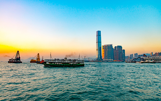 Evening view of Kowloon downtown and its skyscrapers seen from Hong Kong island. Boats passing by at the Victoria Harbor in front.