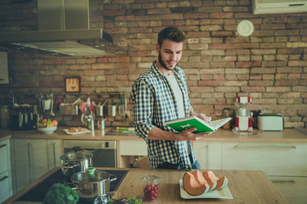 istock Smiling bachelor following recipe from a cookbook in the kitchen. 921593966