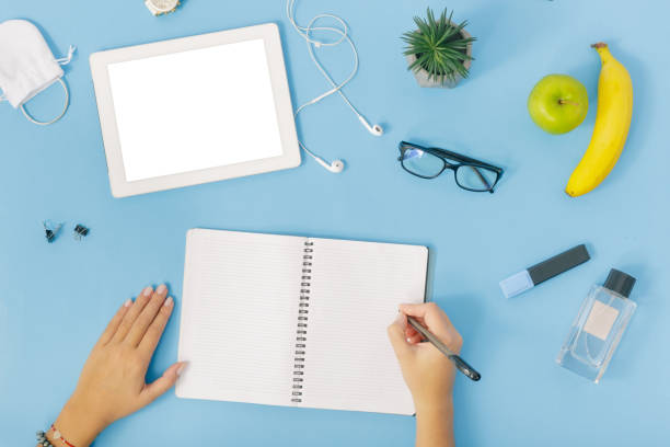 istock Office desk workspace. Female hands write in notebook on blue background. feminine workplace flat lay, top view 921602420