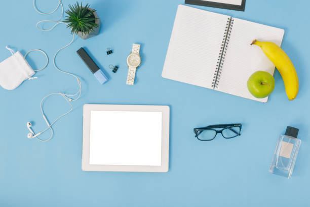 istock Feminine office workspace concept. White tablet, notebook, spectacles, fruit, perfumes, bracelet, felt-tip pen, watches and headphones. Flat lay, top view 921602432