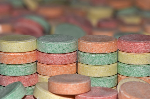 A colorful image showing four stacks of common antacid pills with scattered pills in the foreground and background.