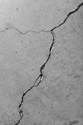 Closeup detail of a weathered cement floor with diagonal cracks.