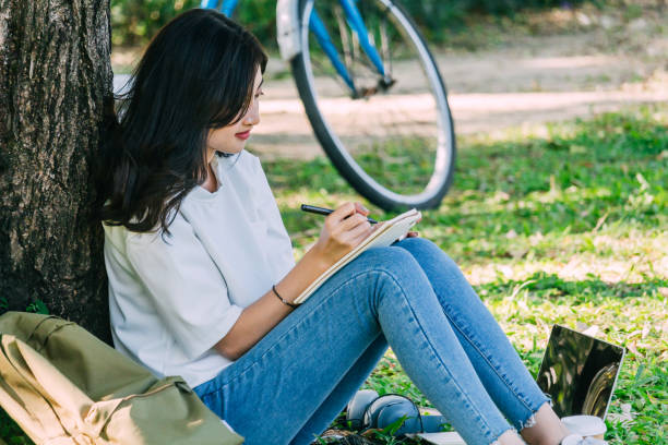 istock Woman with pen writing on a notebook sitting on grass in park 921617620