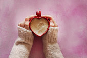 Young woman holding a heart shaped coffee cup on pink background
