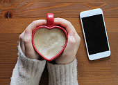 Young woman holding a heart shaped coffee cup on wooden background