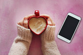 Young woman holding a heart shaped coffee cup on pink background