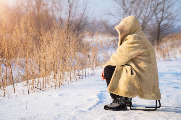 istock Man sits in a fur coat on snowy plain 921621592