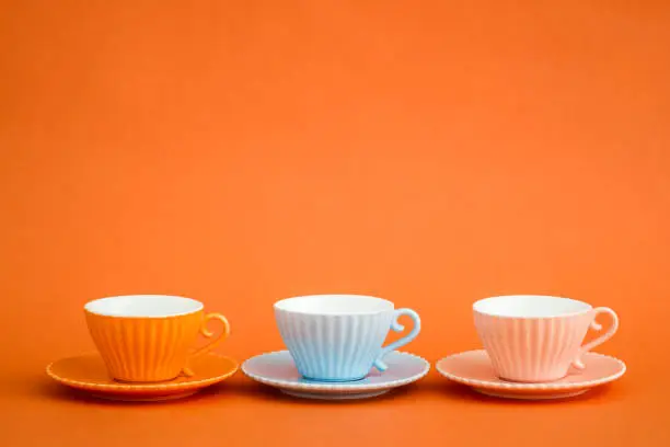 Cute colorful coffee cups on orange background with copy space