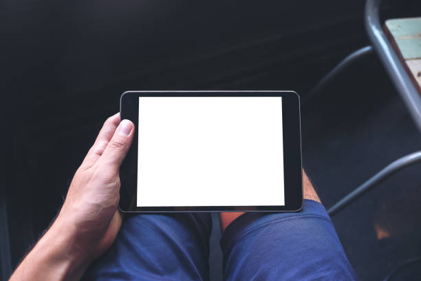 istock Mockup image of a man's hand holding black tablet pc with blank white screen on thigh 921639312