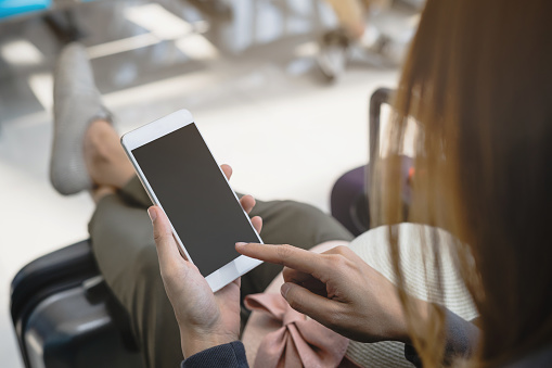 Young asian woman using smart phone while waiting for her flight at the airport