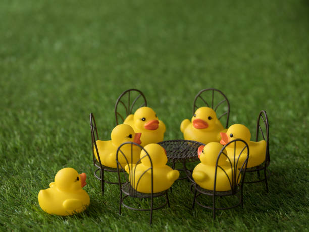 istock Group of five yellow rubber ducks sitting on chairs around a table, scene set on artificial grass. 921680860
