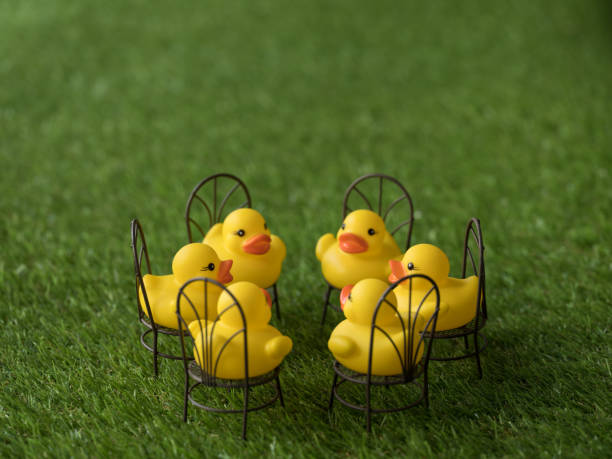 istock Group of six yellow rubber ducks sitting on chairs facing each other, scene set on artificial grass. 921680862
